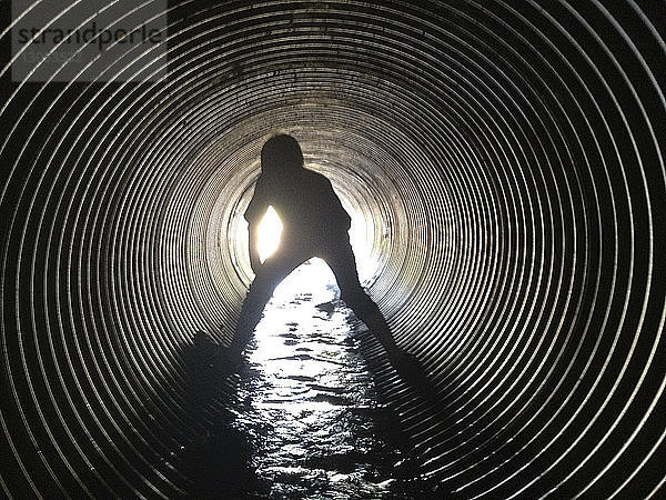 Rückansicht eines im Abwassertunnel stehenden Scherenschnitt-Jungen