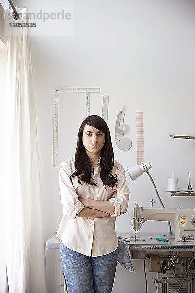 Porträt einer selbstbewussten Modedesignerin  die gegen eine Nähmaschine steht