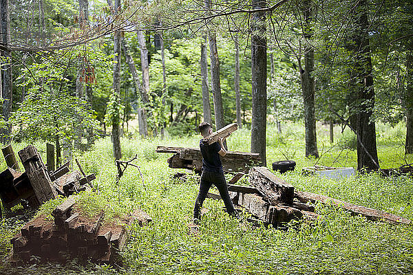 Rückansicht eines Jungen  der Holz trägt  während er auf einem Feld im Wald läuft