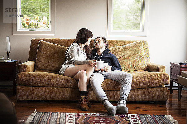 Paar hält Kaffeetassen  während es zu Hause auf dem Sofa sitzt