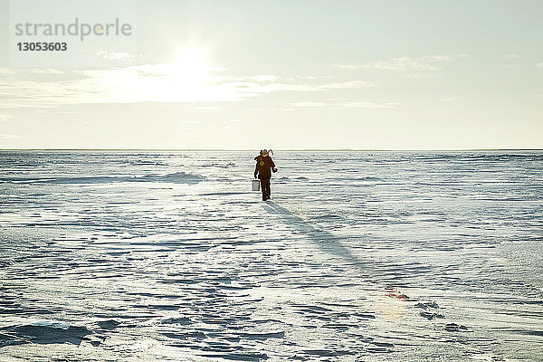 Mann geht auf schneebedecktem Feld gegen den Himmel