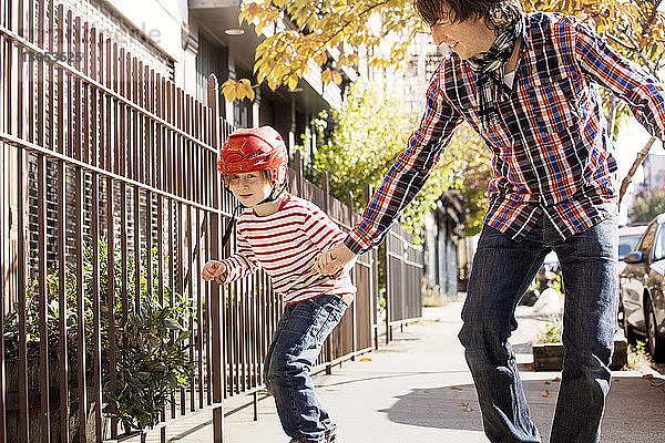 Vater assistiert Sohn beim Skateboarden auf Fussweg