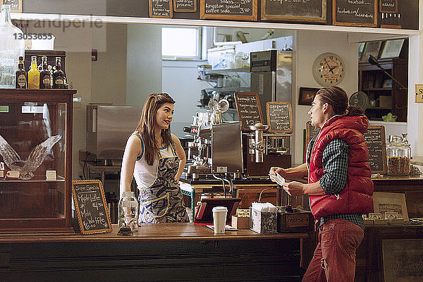 Weiblicher Besitzer schaut Kunden an  während er im Café am Tresen steht