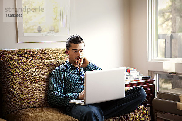 Mann benutzt Laptop-Computer  während er zu Hause auf dem Sofa sitzt