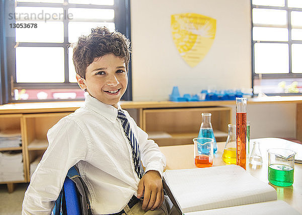 Porträt eines glücklichen Schuljungen  der im Labor am Tisch sitzt