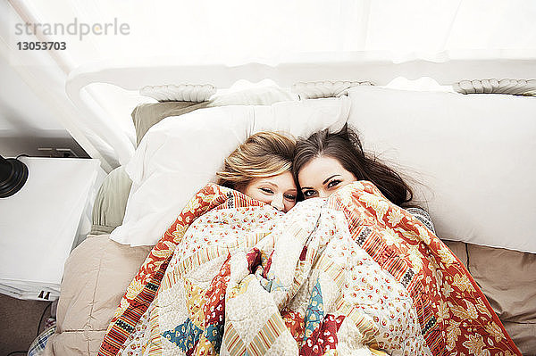 Draufsicht auf Freundinnen  die zu Hause im Bett liegend durch die Decke peppen