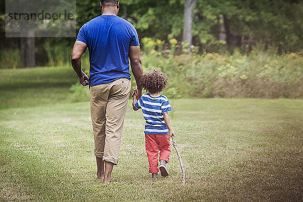Vater und Sohn halten sich beim Gehen auf einem Grasfeld an den Händen