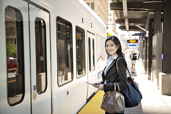 Porträt einer lächelnden Geschäftsfrau  die ein digitales Tablet hält und am Bahnhof steht