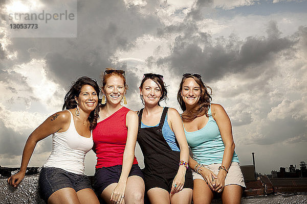 Porträt glücklicher Frauen auf Gebäudeterrasse vor bewölktem Himmel