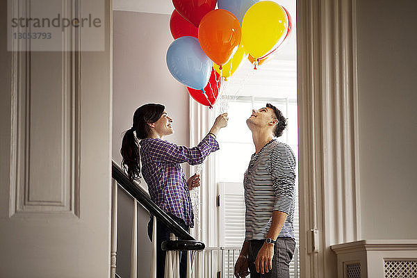 Glückliche Frau hält Heliumballons  während sie zu Hause beim Mann steht