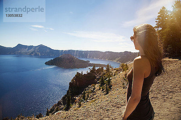 Frau steht auf Klippe  während sie den See gegen den Himmel betrachtet