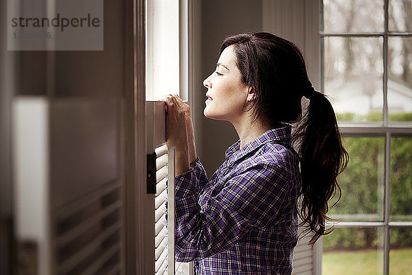 Seitenansicht einer Frau  die durch ein Fenster schaut  während sie zu Hause steht