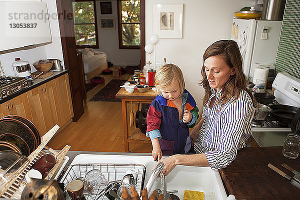Mutter und Sohn waschen Utensilien in der häuslichen Küche