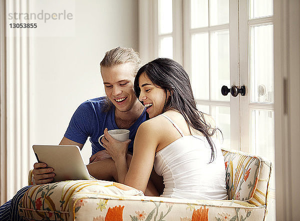 Fröhliches Paar schaut auf Tablet-Computer  während es auf einem Sessel sitzt