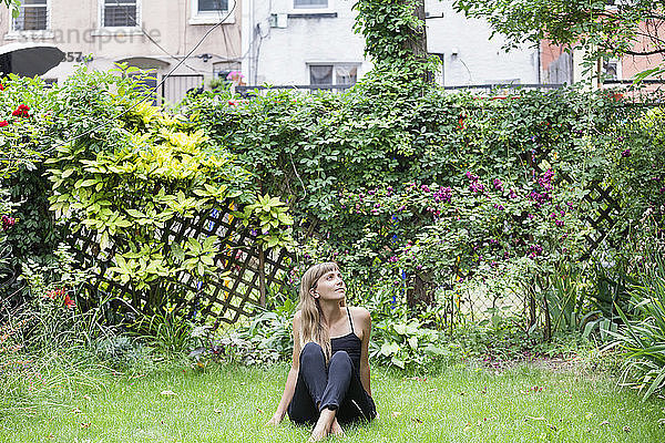 Nachdenkliche Frau sitzt auf einem Grasfeld im Hinterhof