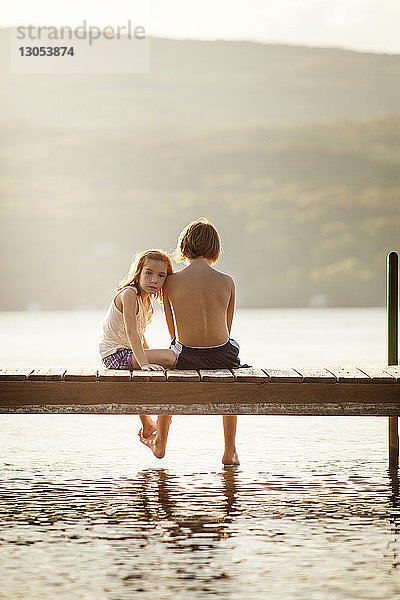 Porträt der Schwester  die mit dem Bruder auf dem Steg über dem See sitzt