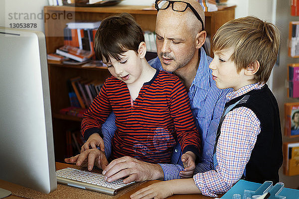 Vater und Söhne nutzen Desktop-Computer zu Hause