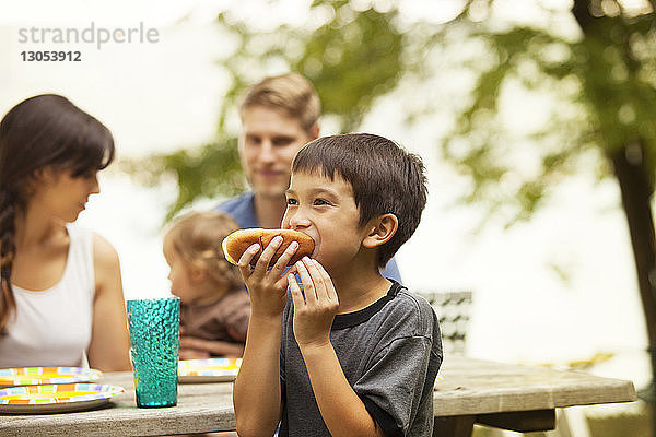 Junge isst Brot gegen Familie  die am Picknicktisch sitzt