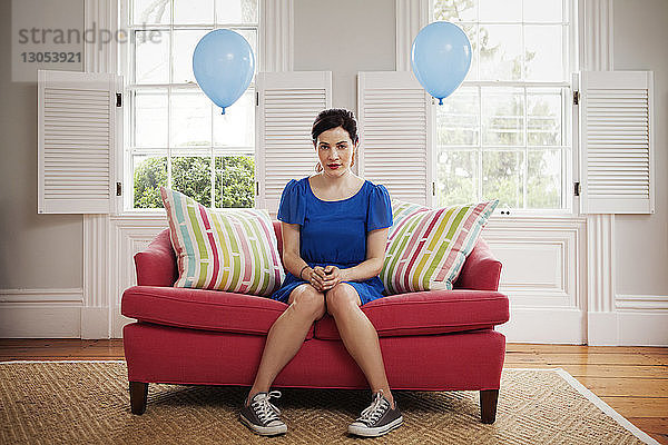 Porträt einer Frau  die zu Hause auf einem Sofa sitzt und an Heliumballons hängt
