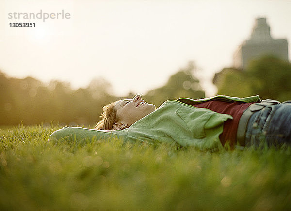 Fröhliche Frau liegt an einem sonnigen Tag auf Grasfeld gegen den Himmel