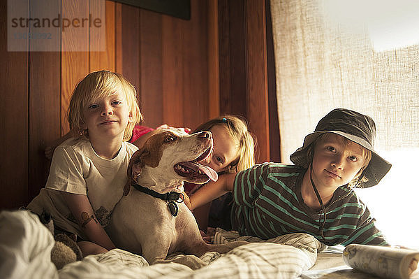 Porträt von Geschwistern mit Hund  die sich zu Hause auf dem Bett ausruhen