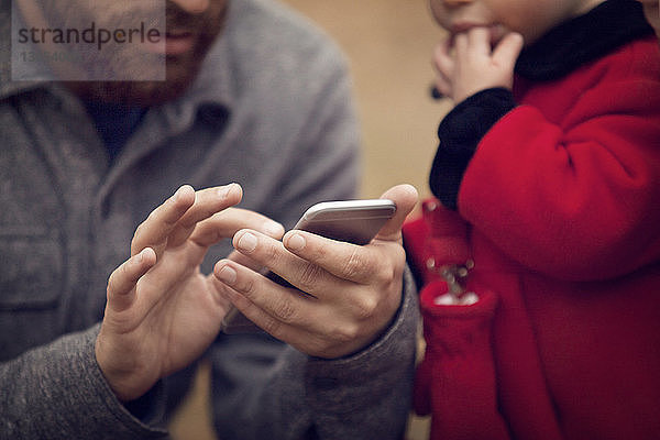 Mittelsektion eines Vaters mit einem kleinen Mädchen  das ein Smartphone im Park benutzt