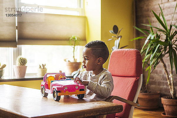 Junge spielt mit Spielzeugauto  während er zu Hause auf einem Stuhl am Tisch sitzt