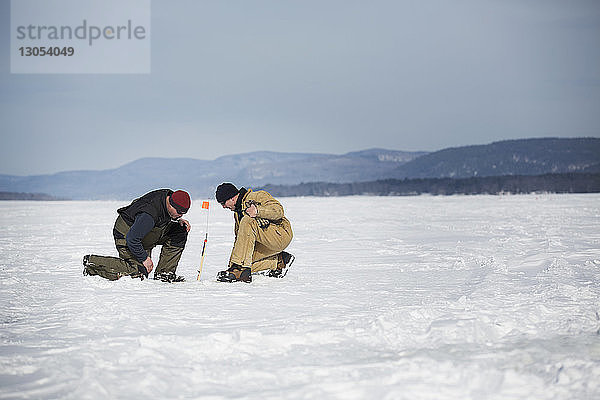 Seitenansicht von Männern beim Eisfischen auf gefrorenem See gegen den Himmel