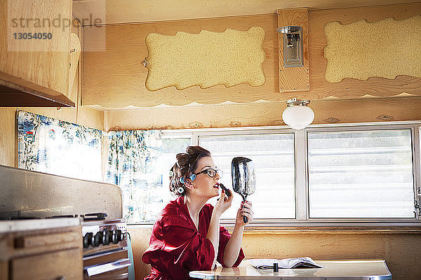 Seitenansicht einer Frau  die Lippenstift aufträgt  während sie im Wohnmobil am Tisch sitzt