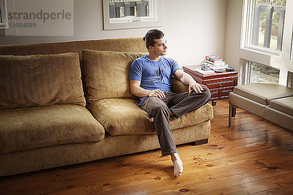Nachdenklicher Mann schaut weg  während er sich auf dem Sofa entspannt
