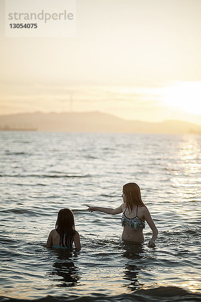 Glückliche Schwestern schwimmen bei Sonnenuntergang im Meer