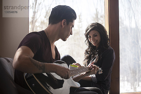 Mann spielt Gitarre  während die Frau auf dem Fensterbrett sitzt