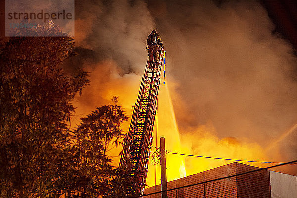 Rückansicht eines Feuerwehrmannes  der Wasser auf ein brennendes Gebäude sprüht