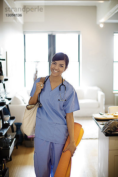Porträt einer lächelnden Ärztin mit Umhängetasche zu Hause stehend