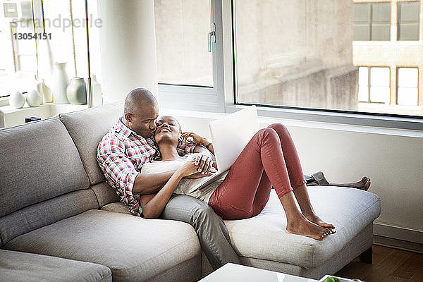 Mann küsst Frau  während er sich zu Hause auf dem Sofa entspannt