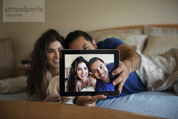 Glückliches Paar  das sich beim Entspannen im Bett über einen Tablet-Computer selbstständig macht