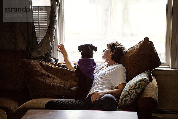 Mann und Hund schauen durchs Fenster  während sie zu Hause auf dem Sofa sitzen