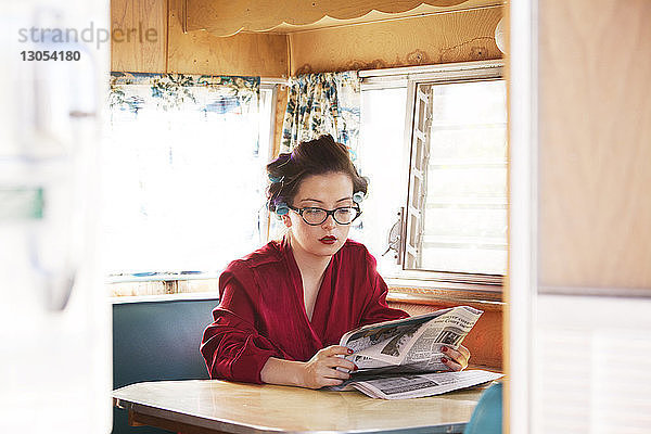 Frau liest Zeitung  während sie im Wohnmobil am Tisch sitzt