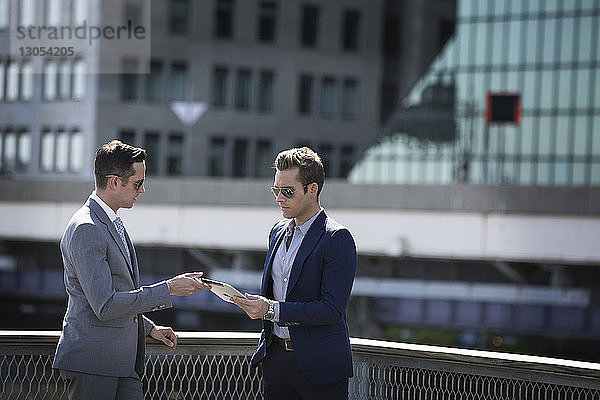 Geschäftsleute  die einen Tablet-Computer benutzen  während sie an einem Geländer vor Stadtgebäuden stehen