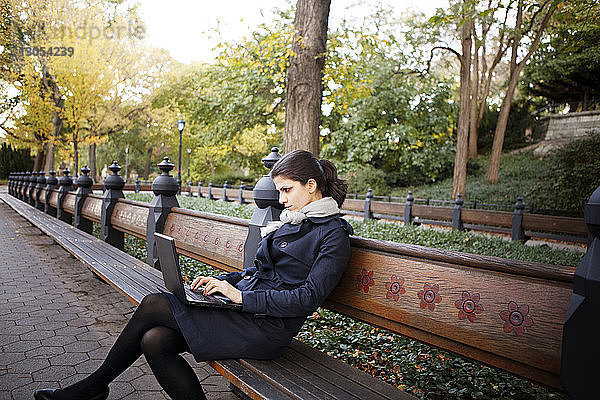 Frau benutzt Laptop  während sie im Central Park auf einer Bank sitzt