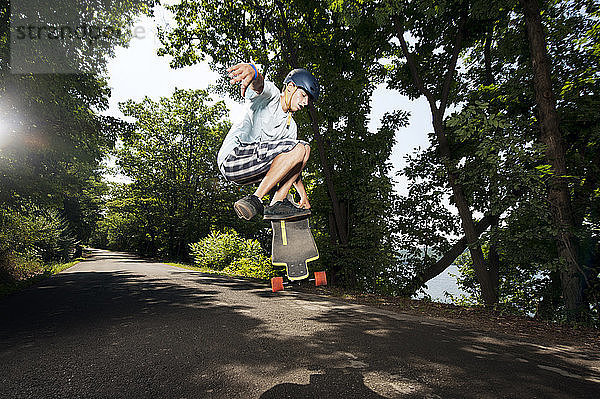 Teenager führt Stunt mit Skateboard über Straße gegen Bäume aus