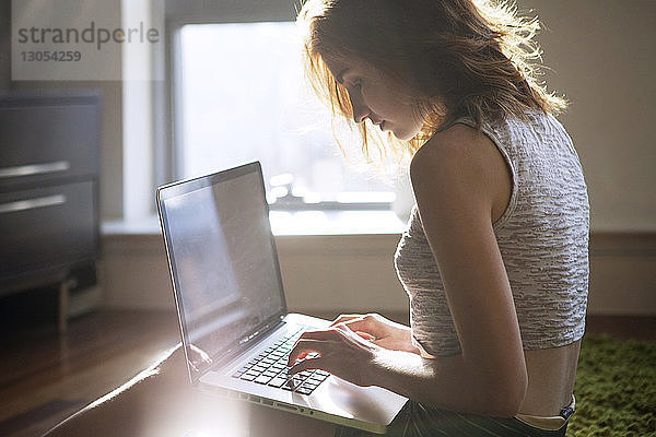 Seitenansicht einer Frau  die zu Hause am Laptop sitzt