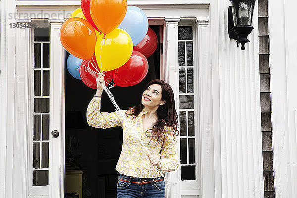 Frau hält Heliumballons  während sie vor dem Haus steht