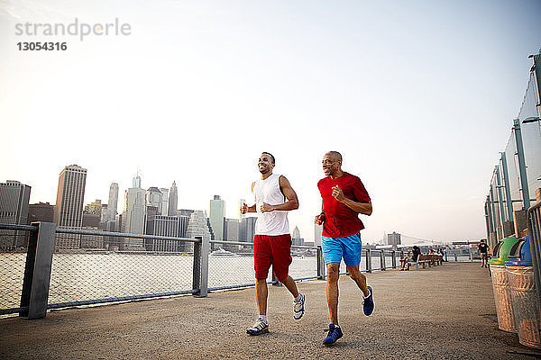 Glücklicher Mann und Vater joggen auf der Promenade am East River in der Stadt bei klarem Himmel