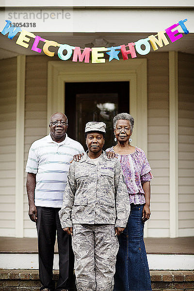 Porträt einer Soldatin  die mit ihren Eltern vor dem Haus steht