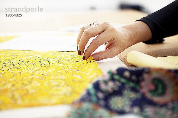 Beschnittenes Bild einer Modedesignerin  die Stoff auf dem Schreibtisch kontrolliert