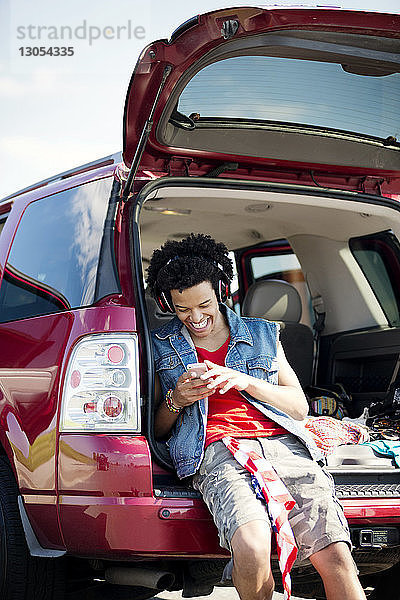 Glücklicher Mann telefoniert  während er im Kofferraum eines Autos sitzt