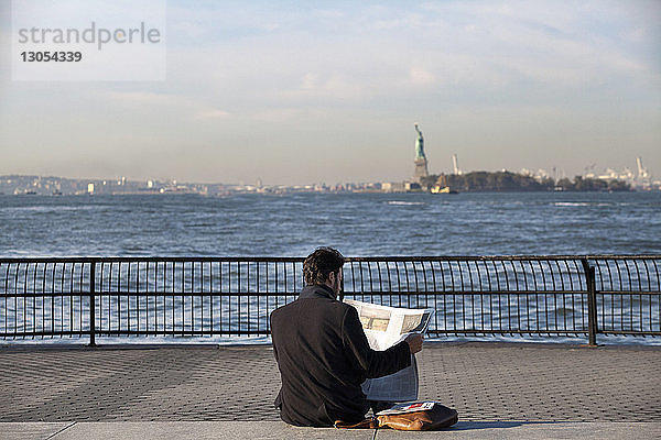 Mann liest Zeitung  während er auf der Promenade am Hudson River sitzt