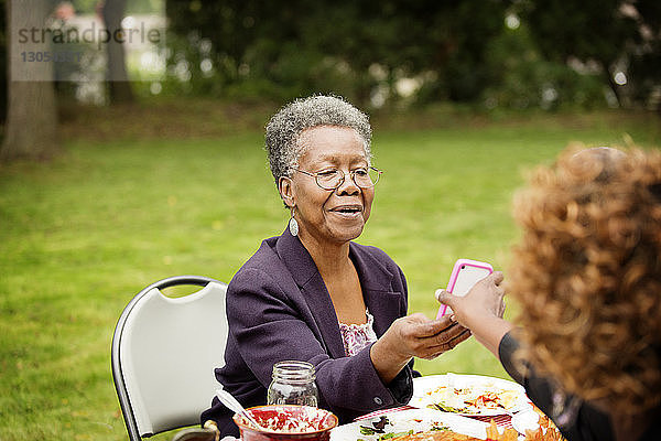 Ausgeschnittenes Bild einer Frau  die der Mutter am Tisch im Hinterhof ein Handy zeigt