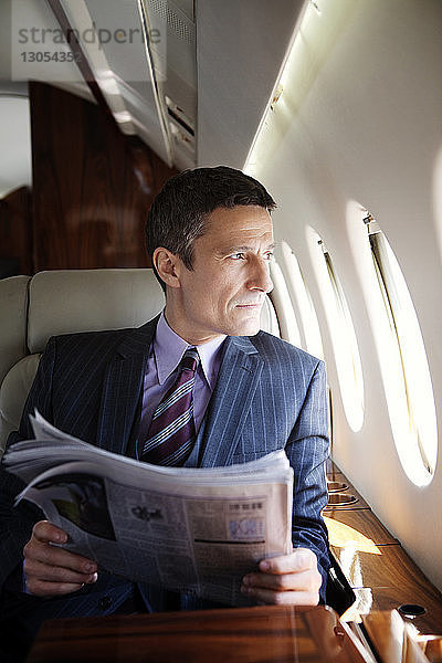 Nachdenklicher Geschäftsmann hält Zeitung  während er im Firmenjet reist